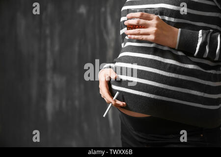 Femme enceinte avec verre d'alcool et de cigarettes sur fond sombre Banque D'Images