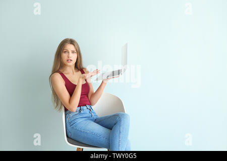 Surpris young woman with laptop sitting on chair contre fond couleur Banque D'Images