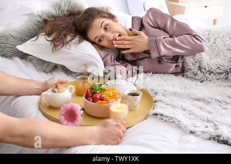 Jeune femme qui reçoit un petit déjeuner au lit de son mari bien-aimé Banque D'Images