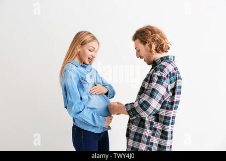 Jeune femme enceinte et son mari la comparaison de taille de leurs ventres sur fond clair Banque D'Images