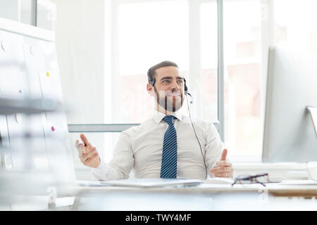 Beau confiant positives avec l'opérateur hotline beard assis à un bureau avec ordinateur et répondre aux appels entrants sur le casque Banque D'Images