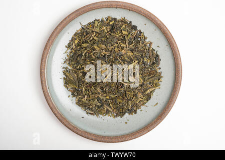 Un produit studio shot d'un tas de feuilles de thé vert chinois séché sur grès émeraude ronde situé sur un arrière-plan uni, blanc. Banque D'Images