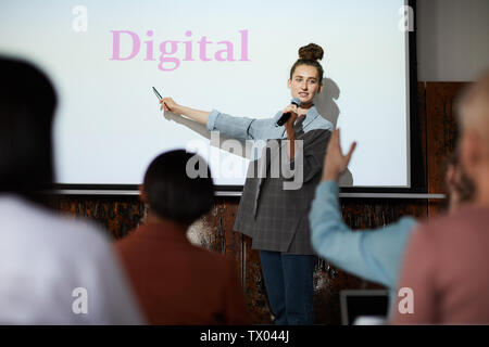 Portrait de jeune femme contemporaine présentation donnant au pointage sur l'écran du projecteur numérique word lors de conférence, copy space Banque D'Images