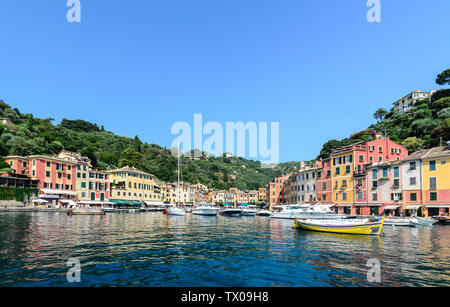 Les bateaux et les bâtiments de Portofino reflétée dans le port avec les montagnes et un ciel bleu en arrière-plan. Banque D'Images