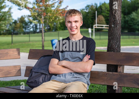 Heureux adolescent assis sur le banc en bois qui se trouve à côté d'un terrain de soccer/football. Banque D'Images