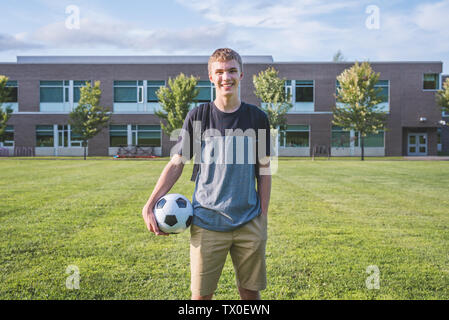 Teenager holding un ballon de soccer et souriant à la caméra. Banque D'Images