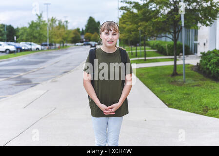 Teenage Girl standing on sidewalk qui passe le long de la face d'une école. Banque D'Images