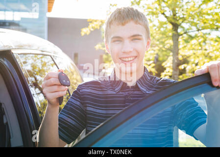 Adolescent heureux de montrer ses clés de voiture qu'il se tient près de sa voiture. Banque D'Images