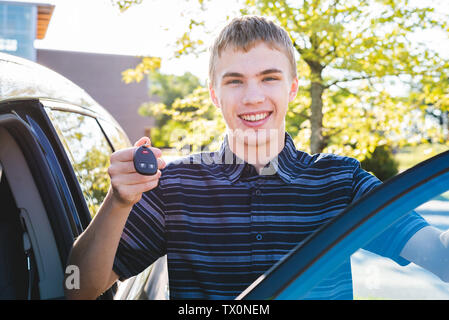 Adolescent heureux de montrer ses clés de voiture qu'il se tient près de sa voiture. Banque D'Images