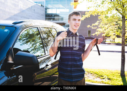 Adolescent debout à côté de sa voiture et mettre sur son sac à dos avant de l'école. Banque D'Images