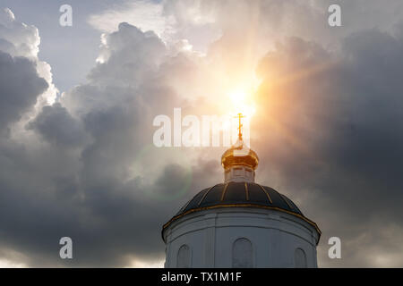 Les rayons du soleil font leur chemin à travers les nuages orageux éclairant la croix d'or sur le dôme de l'ancienne église Banque D'Images