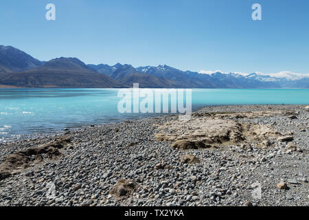 Plage en pierre vide près de l'eau et de montagnes de neige dans le ciel bleu Banque D'Images