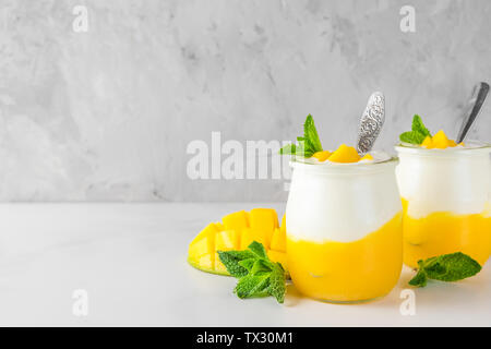 Deux verres de mangue yogourt avec fruits frais, de menthe et de cuillères sur fond de béton. petit-déjeuner sain. close up Banque D'Images