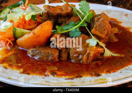 Un curry de mouton roti avec sambals - un repas composé de Durban d'un roti surmontée de mutton curry et sauce. La carotte râpée sont sambals avec c Banque D'Images