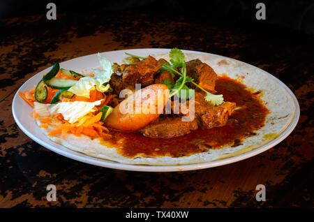 Un curry de mouton roti avec sambals - un repas composé de Durban d'un roti surmontée de mutton curry et sauce. La carotte râpée sont sambals avec c Banque D'Images