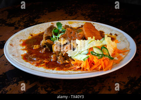 Un curry de mouton roti avec sambals - un repas composé de Durban d'un roti surmontée de mutton curry et sauce. La carotte râpée sont sambals avec c Banque D'Images