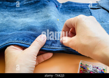 Femme broche pliée en deux mains jeans bleu avant de couper. Jeans avec un grand trou sur un pantalon en dessous du genou. Faire denim shorts. Sur une zone orange Banque D'Images