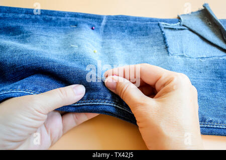 Mains femme broche pliée en deux eans avant de couper. Jeans avec un grand trou sur un pantalon en dessous du genou. Ce short en jean bleu. Sur une orange backg Banque D'Images