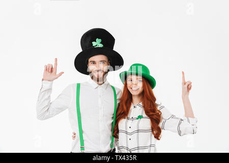 Happy young couple portant des costumes, la célébration de saint Patrick Day isolated over white background, pointer du doigt Banque D'Images