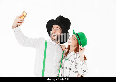 Happy young couple portant des costumes, la célébration de saint Patrick Day isolated over white background, en tenant un selfies Banque D'Images