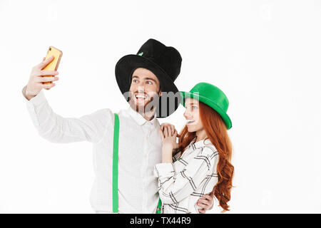 Happy young couple portant des costumes, la célébration de saint Patrick Day isolated over white background, en tenant un selfies Banque D'Images
