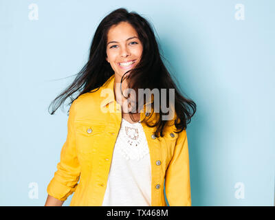 Portrait de jeune femme aux cheveux noirs portant veste jaune, fond bleu clair Banque D'Images