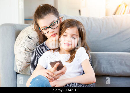 Deux soeurs assis en face de la table looking at smartphone Banque D'Images