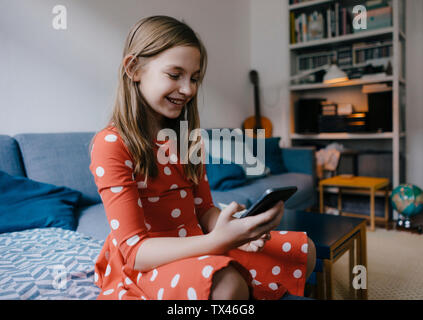 Happy girl sitting on sofa at home using cell phone Banque D'Images