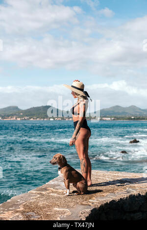 Espagne, Majorque, femme tatouée debout à côté de son chien regardant la mer Banque D'Images