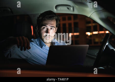 Jeune homme avec portable en voiture à la nuit Banque D'Images