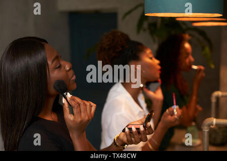 Trois amis appliquant le maquillage au Ladies' room Banque D'Images