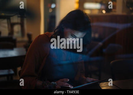 Jeune femme assise à table dans un restaurant à l'aide de tablet Banque D'Images