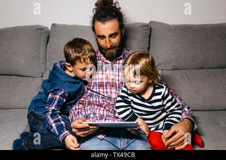 Père assis sur le canapé avec ses enfants à regarder des films sur tablette numérique Banque D'Images