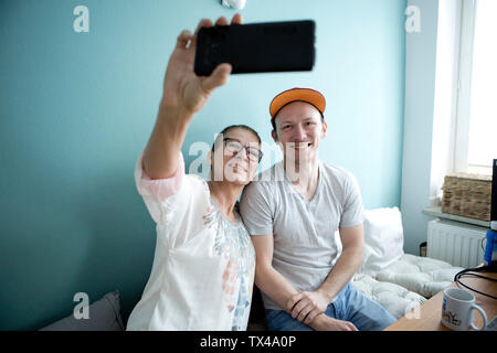 La mère et le fils assis à la table de cuisine, en tenant vos autoportraits smarrtphone Banque D'Images