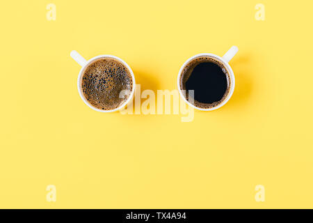 Un minimum de mise à plat de la composition de deux tasses de café noir sur fond jaune avec copie espace, vue de dessus. Banque D'Images