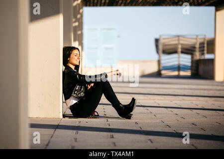 Young woman sitting on floor, profitant de la lumière du soleil Banque D'Images