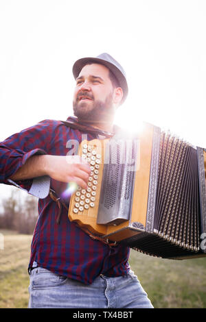 Portrait d'homme barbu jouant à l'accordéon sur un pré à rétro-éclairage Banque D'Images