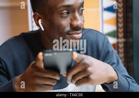 Jeune homme souriant avec des écouteurs sans fil et un téléphone cellulaire Banque D'Images