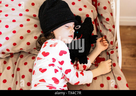 Little girl wearing cap dormir dans le lit avec son doudou Banque D'Images