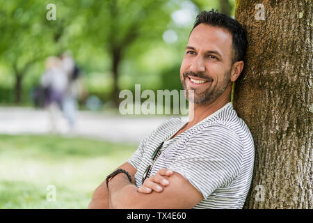 Portrait of smiling man leaning against a tree in park Banque D'Images