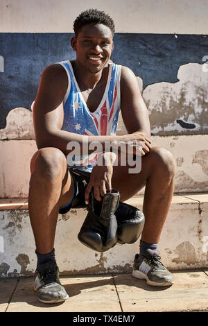 Portrait of smiling boxer avec ses gants de boxe assis en plein air après la formation Banque D'Images