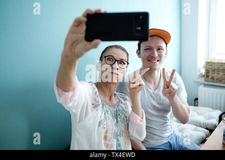 La mère et le fils assis à la table de cuisine, en tenant vos autoportraits smarrtphone Banque D'Images