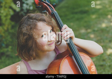 Une jeune fille souriante avec le violoncelle dans jardin Banque D'Images