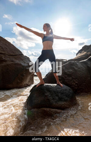 Seychelles, Mahe, la plage de Takamaka, young woman doing yoga on a rock Banque D'Images