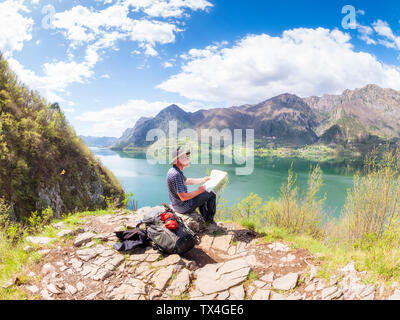 L'Italie, la Lombardie, le printemps au lac d'Idro, randonneur assis avec la carte au point d'observation Banque D'Images