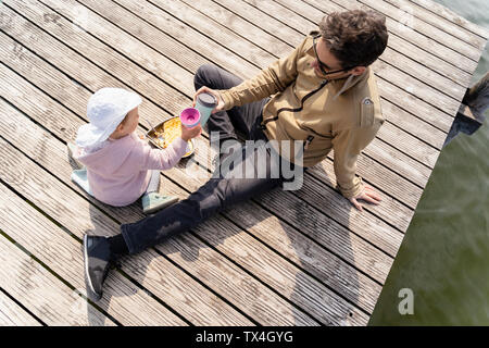 Allemagne, Bavière, Ostfildern, père et fille se détendre sur jetty ayant un snack Banque D'Images