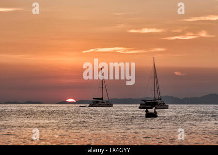 La Thaïlande, Krabi, Railay beach, bateaux flottant sur l'eau au coucher du soleil Banque D'Images