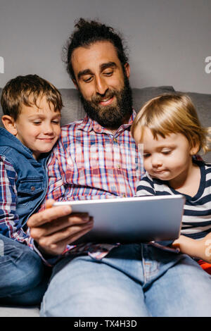 Portrait du père assis sur le canapé avec ses enfants à regarder des films sur tablette numérique Banque D'Images