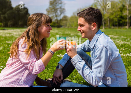 Jeune couple toastin avec du jus de fruits dans un parc Banque D'Images