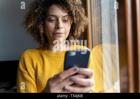 Femme dans un pull jaune, using smartphone Banque D'Images